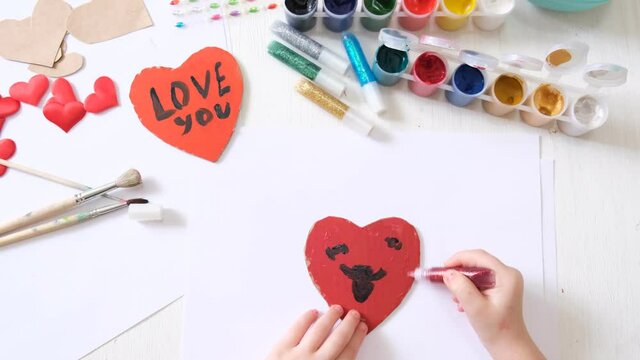 Child making homemade greeting card. A little girl paints  hearts as a gift for Mothers Day or Valentines day . Traditional play concept. Arts and crafts concept.