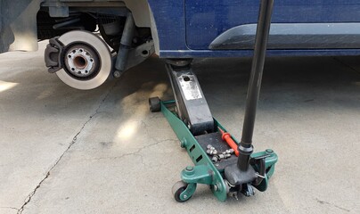 A jack lifts up a car during tire replacement. View of car disc brake during changing a tire.