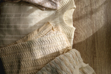 White and beige sweaters on wooden background, illuminated by sunlight. Flat lay.