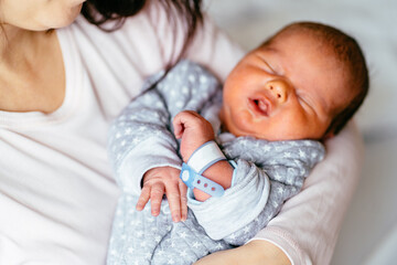 Middle age mother supports and tenderly cuddles the newborn baby boy gently while the infant is...