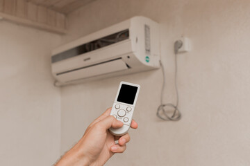 Fototapeta premium The guy's hand holds the remote control of the air conditioner. Cooling and temperature control in the room of the house