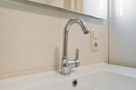 Sink faucet in modern bathroom interior under mirror