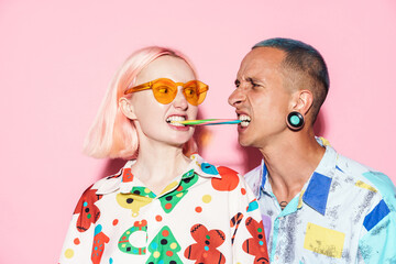 Young couple in multicolored shirts grimacing while eating chewing candy