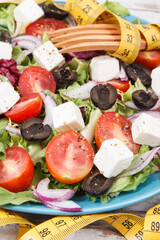 Tape measure and greek salad with feta cheese and vegetables as healthy meal containing vitamins