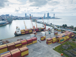 Drone view of the loading of containers on a ship in the Batumi industrial seaport against the background of the city. Georgia - obrazy, fototapety, plakaty