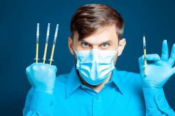 A doctor in a medical mask and gloves, in a blue uniform with thin syringes between his fingers