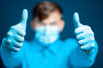 A doctor in a medical mask and gloves, in a blue uniform, shows a thumb up
