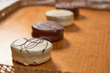Argentinian traditional alfajores covered with brown and white chocolate on a rustic wooden tray.
