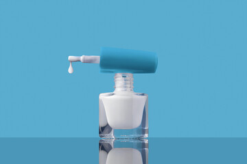 White nail polish bottle and drop on brush on blue background. Cosmetics concept.