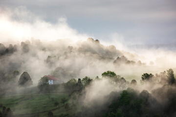 House on hill with clouds and fog over mountains during sunrise in the Vosges, France