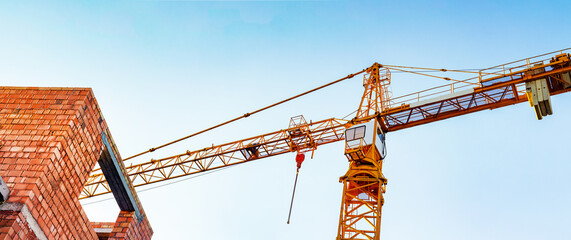 Photo of orange colored building crane on blue sky background. - Powered by Adobe