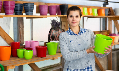 Young woman amateur gardener choosing pots for growing plants in floral and garden supplies store