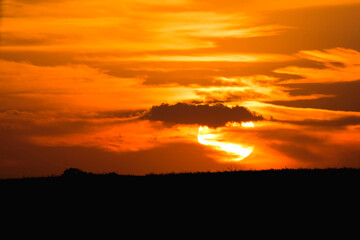 A dramatic sunset, sun behind clouds and an orange sky