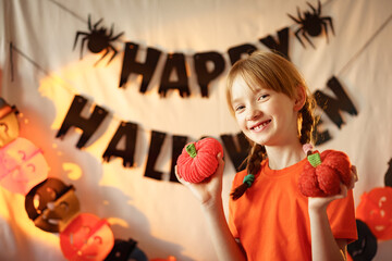 girl with pigtails having fun on a background of Halloween attributes. knitted orange pumpkins. preparation for the holiday. garlands on the walls.