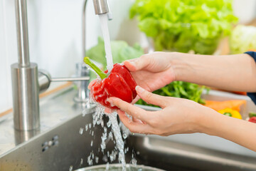 Close up asian young housekeeper woman,  washing sweet pepper, red paprika, vegetables with splash water in basin of water on sink in kitchen, preparing fresh salad, cooking meal. Healthy food people.