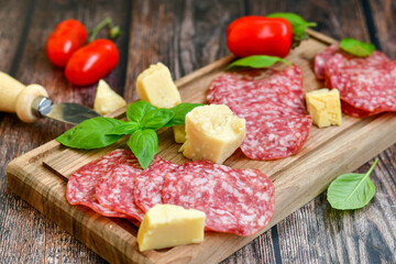 Italian  dried thinly sliced   artisan  pork salami Milano , parmesan cheese, tomatoes   and fresh basil on wooden background .Rustic  home made italian snack.
