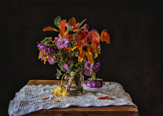 Autumn flowers in glass jar on wooden surface covered with white tablecloth