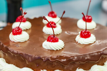 Chocolate frosted round cake with cherries and whipped cream decorating the top.
