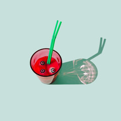 A glass filled with red drink, with eye balls in the liquid and two green straws. Pastel mint background. Spooky Halloween traditional celebration concept.
