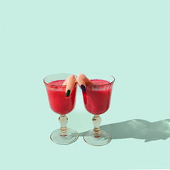 Two wine glasses filled with red liquid and a finger coming out of each glass. Mint green background. Spooky Halloween party invitation concept.