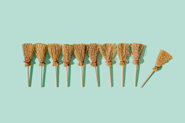 Ten brooms aligned on pastel green background, one is falling out of the line. Witchcraft Halloween...