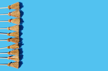 Ten brooms neatly aligned on the left side on a blue background. Halloween witchcrafts party creative concept or invitation.