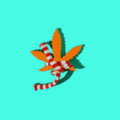 Obraz premium An orange maple leave with a striped red and white scarf. Pastel green background. Minimal romantic Autumn creative concept. Surreal fall background or banner