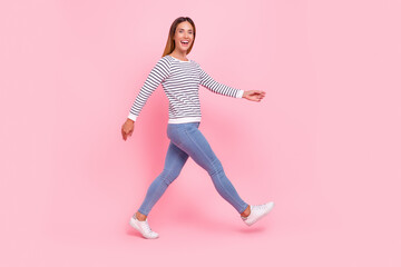 Photo of funny shiny young woman dressed striped pullover walking smiling isolated pink color background