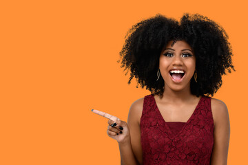 Positive young woman with afro hairdo, points to the side with a cheerful expression, shows...