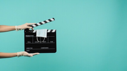 hand is holding black clapperboard with face mask on green mint background.