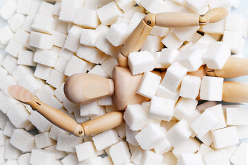 A wooden mannequin doll, strewn with sugar cubes, is drowning in a pile of sugar.Unhealthy concept...