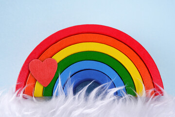 Wooden toy rainbow with a heart on a blue background with white fur, similar to a cloud...