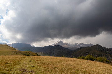 A strong overcast building up above Mount Kazbeg in Caucasus, Georgia. Rainy clouds. There slopes are barren and stony below the snow-capped peak and the Gergeti Glacier. Massive glacier foot