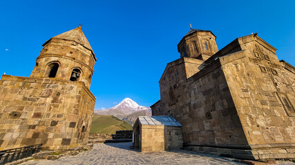 Close up view on Gergeti Trinity Church in Stepansminda, Georgia. The church is located on a high Caucasian mountain. Clear and blue sky above the church. Snow-capped Mount Kazbek in the back