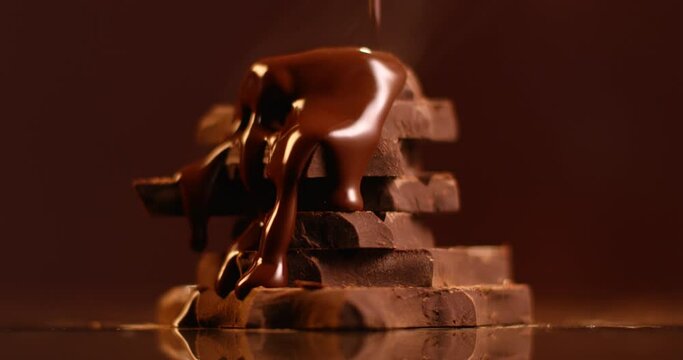 Dark melted chocolate pouring over stack of broken pieces chocolate in slow motion