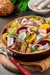 Herring salad. Salad of salted herring, beetroots, potatoes, onions and cucumbers in a bowl on a dark background. Scandinavian cuisine.