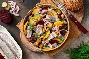 Herring salad. Salad of salted herring, beetroots, potatoes, onions and cucumbers in a bowl on a dark background top view. Scandinavian cuisine.