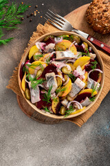 Herring salad. Salad of salted herring, beetroots, potatoes, onions and cucumbers in a bowl on a dark background top view. Scandinavian cuisine. Copy space