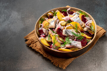 Herring salad. Salad of salted herring, beetroots, potatoes, onions and cucumbers in a bowl on a dark background. Scandinavian cuisine. Copy space