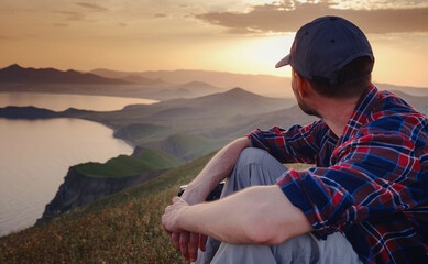 Confident man sitting and enjoying view in hilly landscape far from people. Tourist photographer is relaxing in nature during sunset. Adventure, Travel and Hike concept.