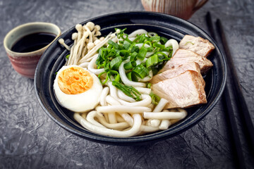 Traditional Japanese udon chicken ramen soup with noodles, enoki and egg served as close-up in a design bowl on a wooden board