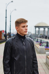 Handsome brutal man in black leather jacket model style. Portrait of a handsome guy on a blurred urban background with a rotunda.