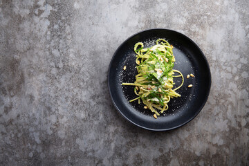 Spaghetti with spinach, pine nuts and parmesan cheese in a black plate on a gray table