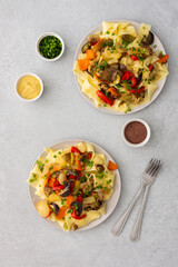 Fettuccine pasta with stewed vegetables, delicious autumn lunch in plates with mustard and fresh green onions