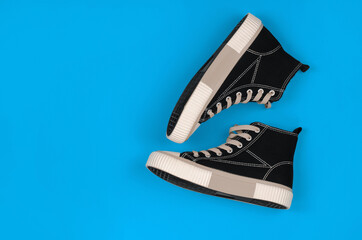 Stylish black sneakers on a blue background with place for text, flat lay. A pair of sports shoes on a colored background.