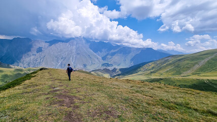 A man standing on a lush pasture in Kazbeg Region in Caucasus, Georgia. Rainy clouds approaching. There are many mountain chains in the back. Vast meadows. Roaming freely