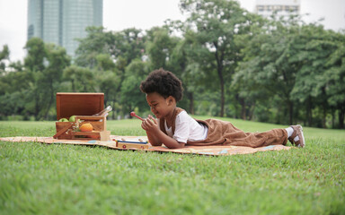 Obraz premium Little African kid boy crying and holding a sore finger when playing xylophone toys alone with sad face at park and lying down on mat with picnic basket on weekend