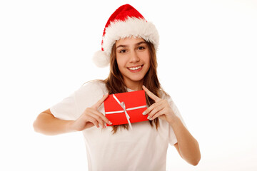 Happy caucasian girl teenager standing in white t-shirt and santa claus red hat holding gift certificate or greeting inviting card over white background. Studio portrait. Christmas and New year 