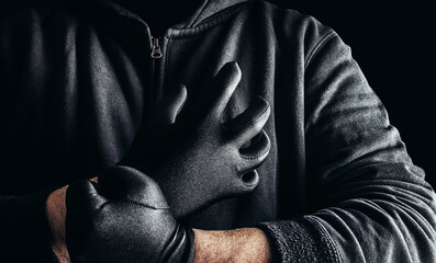 Photo of a stranger stalker man in black hood and clothing putting on gloves on dark background.