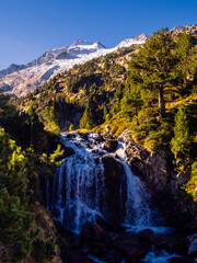 Paisaje alpino con una cascada de primer plano y una montaña nevada de fondo con un cielo azul 